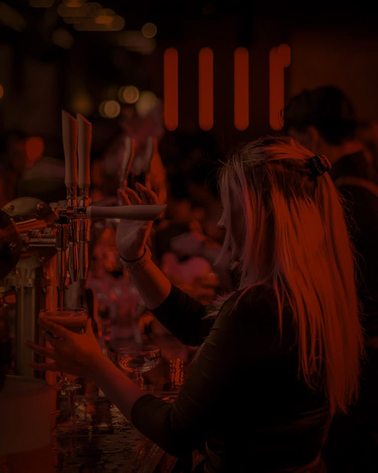 Vrouw tapt een drankje achter de bar in een drukke omgeving