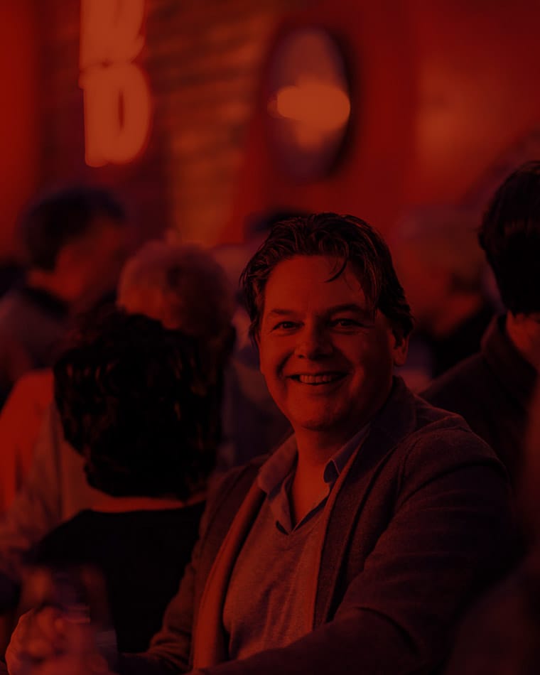 Lachende man in een sfeervolle clubomgeving met een groep mensen op de achtergrond