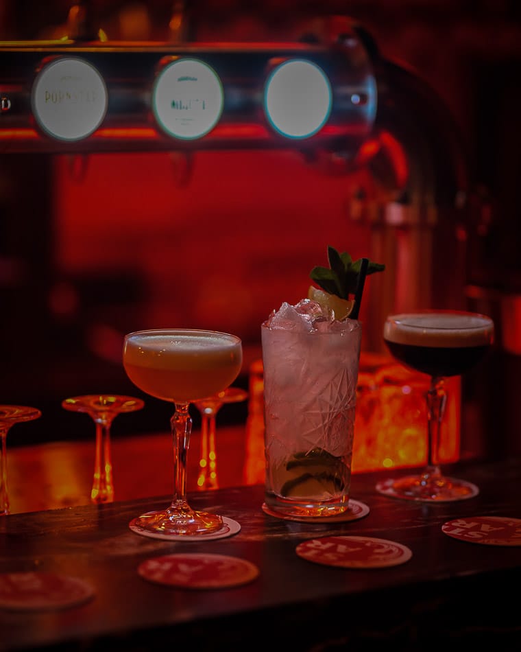 Drie cocktails op een bar met een tapinstallatie op de achtergrond
