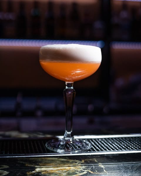 Cocktail in een elegant coupeglas met een schuimlaag, geserveerd op een bar.