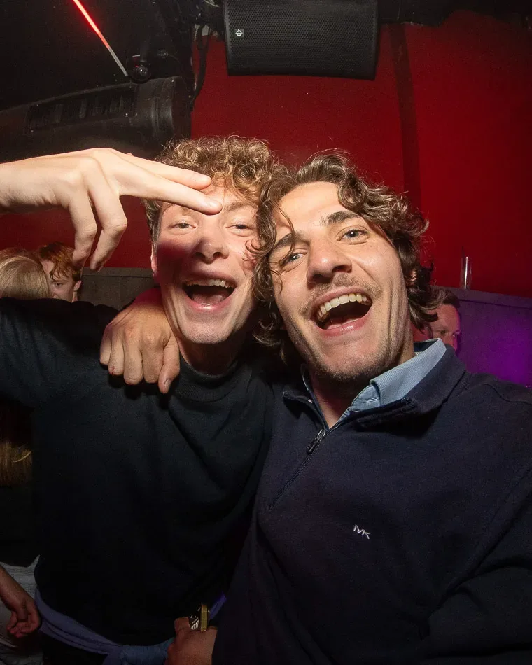 Twee lachende mannen tijdens een cocktailavond in club Roto, met promotekst 'Donderdag' in beeld.